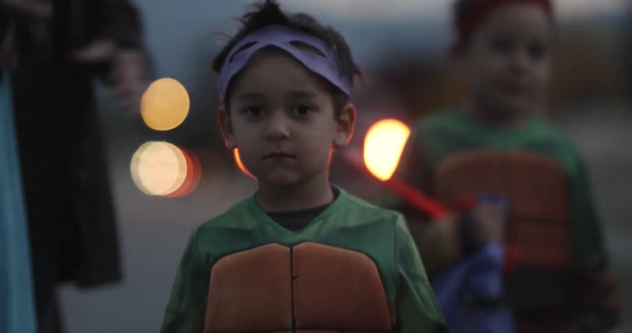 Two children in costumes walk down the street