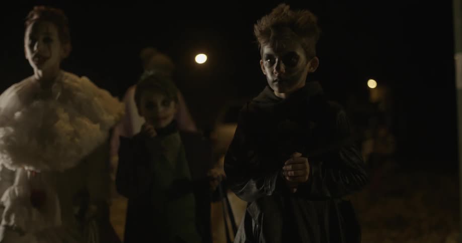 Children in halloween costumes walk down the street at night