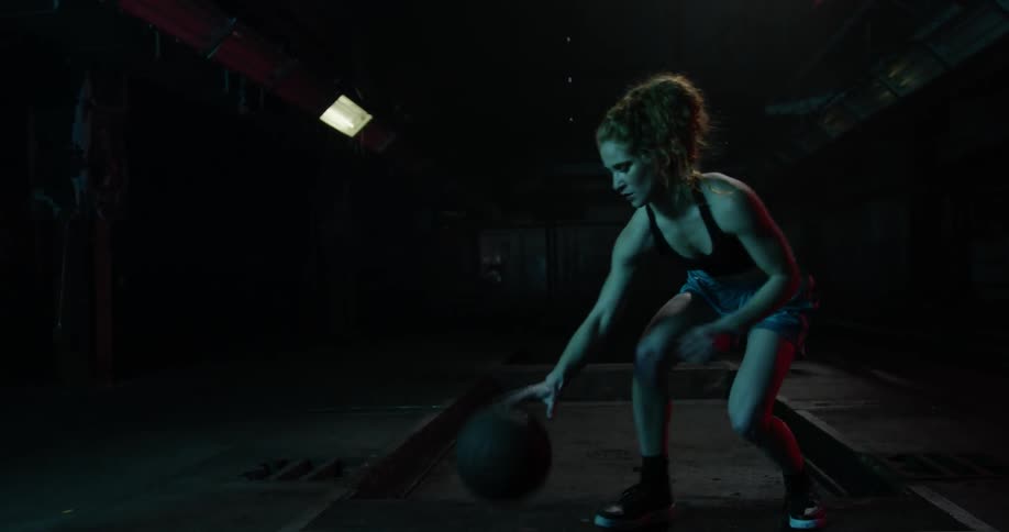 A woman dribbles a basketball in a dark room