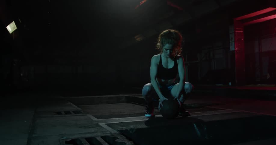 A woman is sitting on a basketball in a dark alley