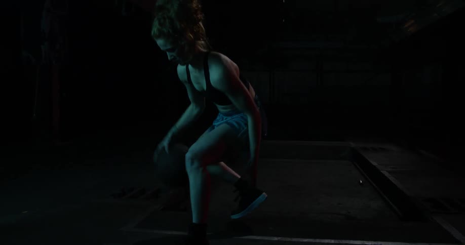 A lady is dribbling a basketball between her legs