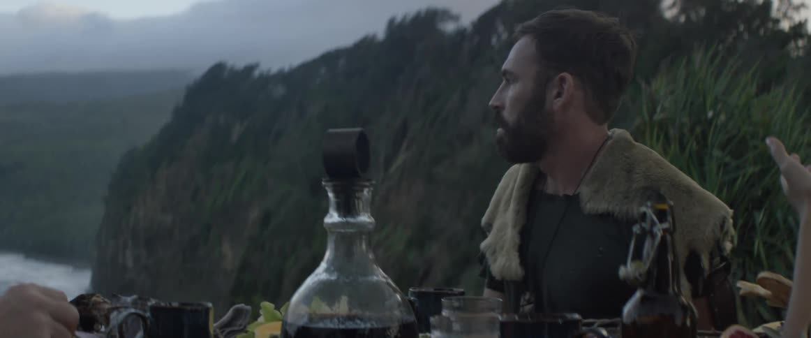 Bearded man wearing a fur pelt sits at a table
