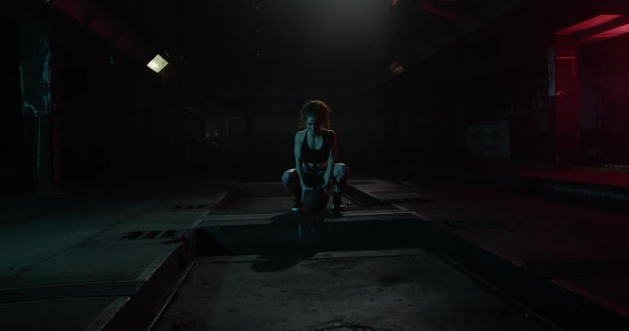 A woman crouches over a basketball in a dark room
