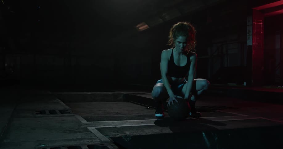 A woman kneels down gripping a basketball
