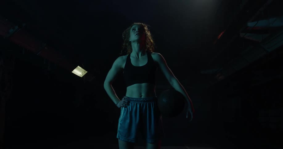 A woman stands in a dim gym holding a ball