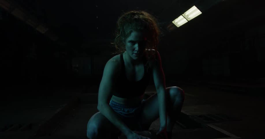 A woman kneels in a dimly lit gym