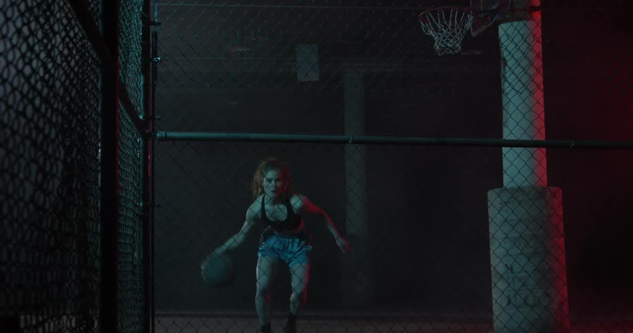 A woman is dribbling a basketball between her legs