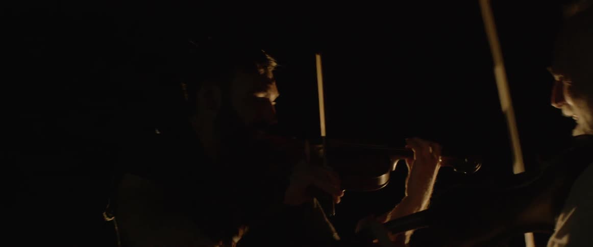 Two men play violin face to face by a campfire