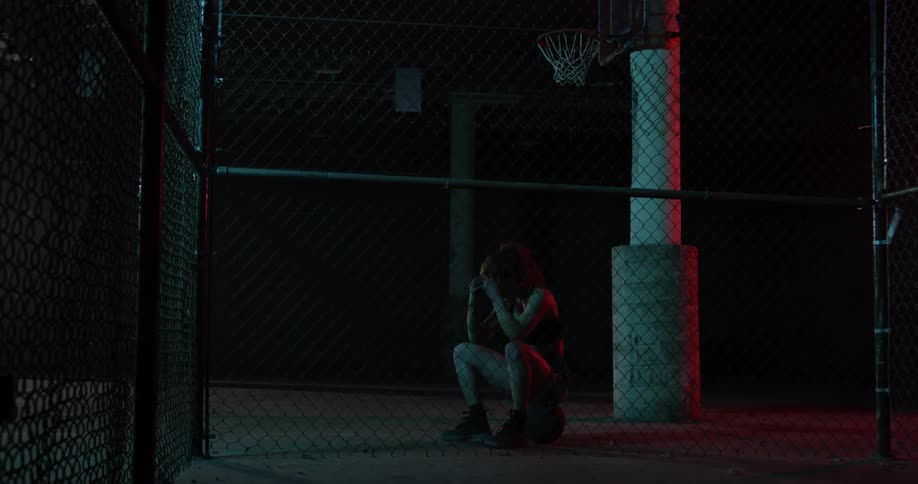 A woman sits on a basketball and holds her head in her hands