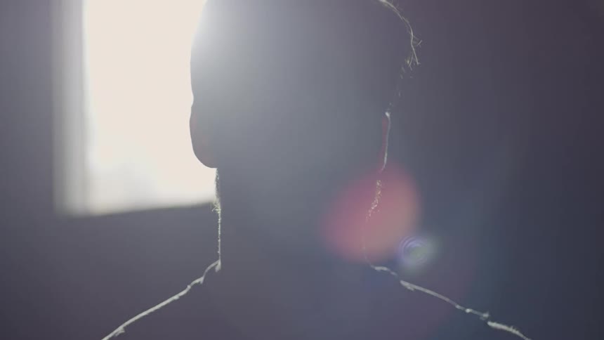 A man is standing in front of a window in a dark room