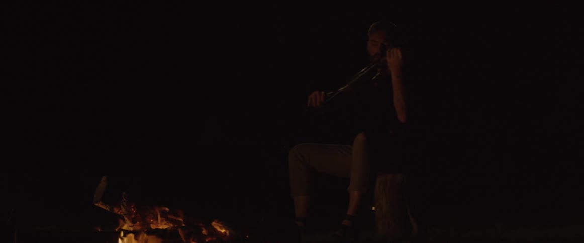 A man plays violin next to a campfire