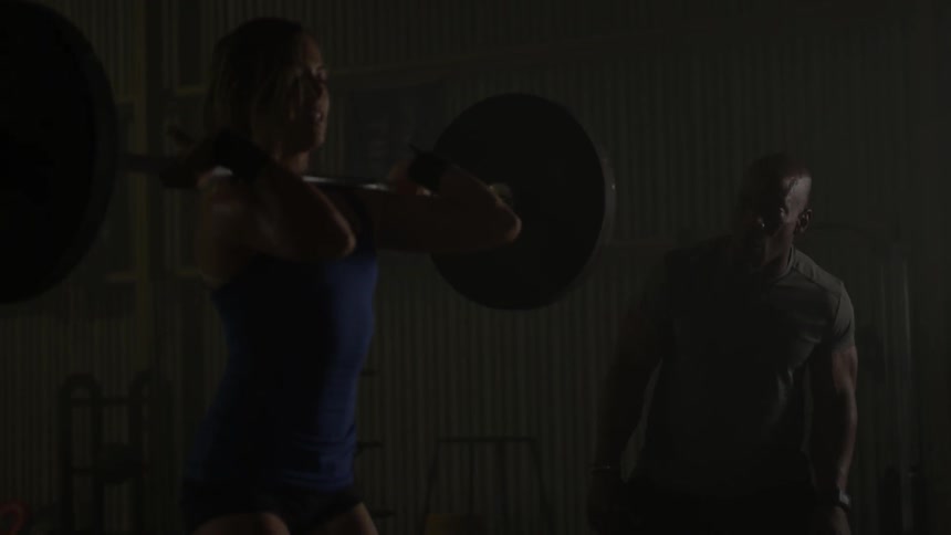 A man instructs a woman who is lifting weights