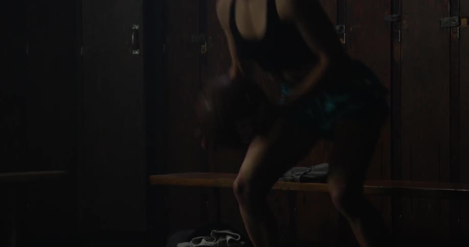 A woman sits in a locker room holding a basketball