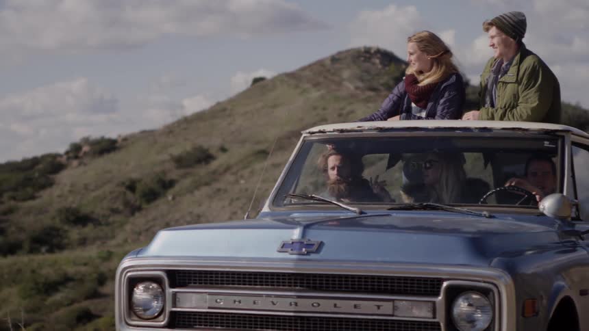 Two people ride in the back of a truck in the daytime