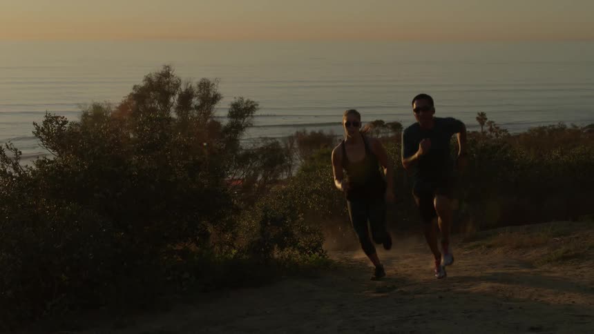 A man and woman jog on the coast at sunset