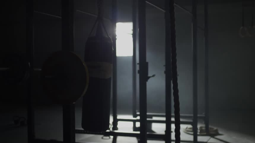 The gym is dark, and the heavy bag is waving back and forth