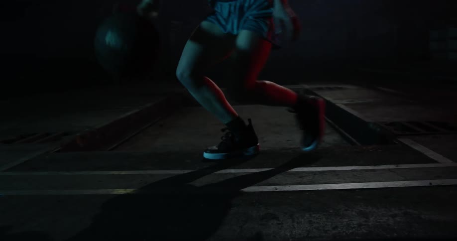 Person dribbling basketball on court at night