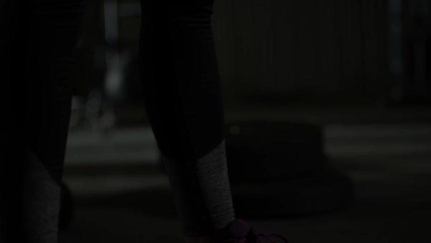 A person lifts a barbell in a dark gym