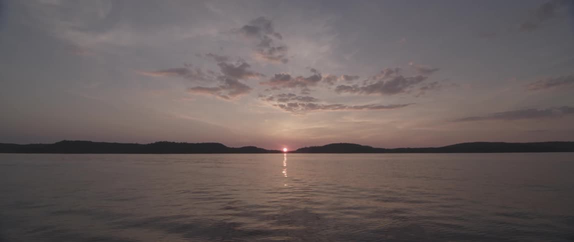 Long shot of a calm lake and a distant sunset behind mountains