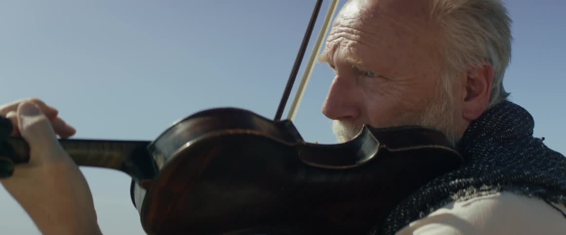 A man is playing the violin while looking off in the distance
