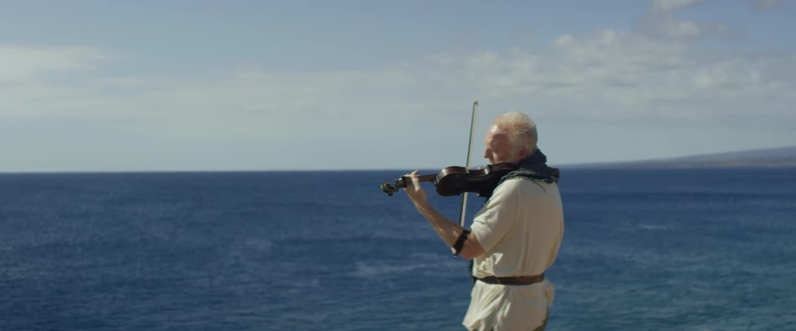A man is playing the violin on the edge of a cliff