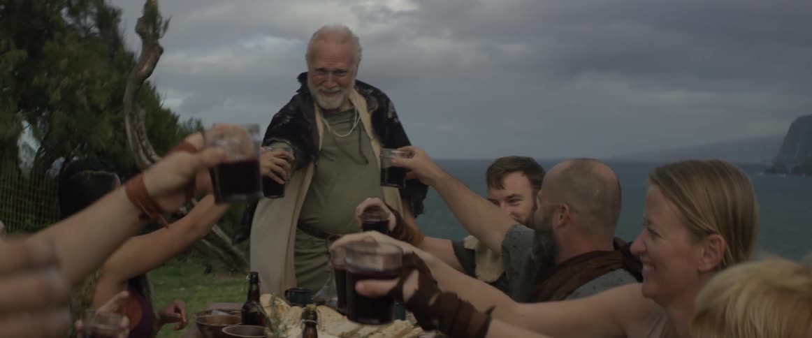 An old man is standing and giving a toast at a dinner party