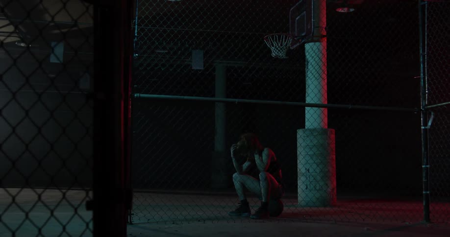 A woman sits by a basketball hoop on her ball