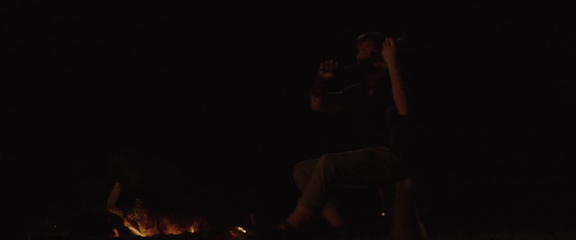 A man plays the violin next to a fire
