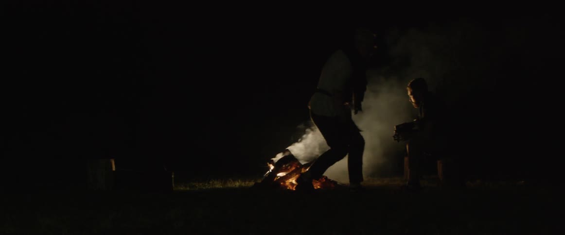 A man walks over to another man at a camp and gives him a violin