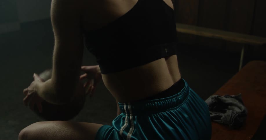 Woman wearing a sports bra bounces a basketball while sitting on a bench