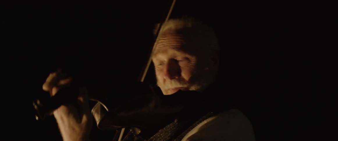 Two men play violins together outside at night