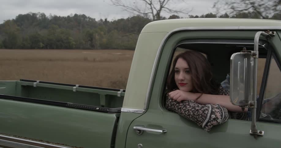 A man and woman drive through the countryside in an old pickup truck