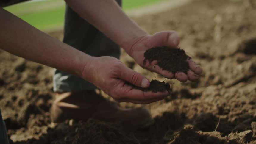 A man kneels in a dirt field and holds soil in his hands
