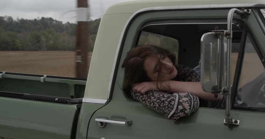 A woman leans out the window of a moving pickup truck