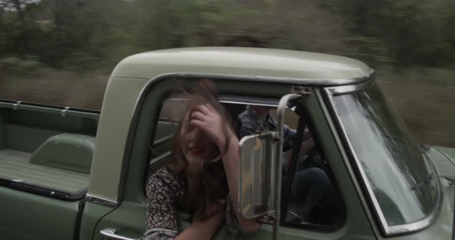 A man and woman ride through the countryside in an old pickup truck