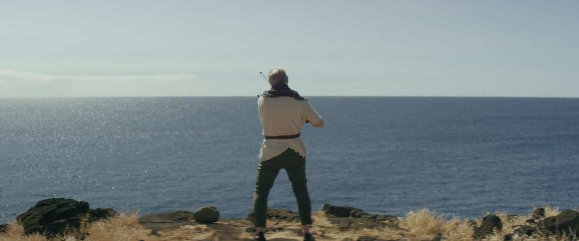 A man plays a violin on a ridge overlooking to ocean