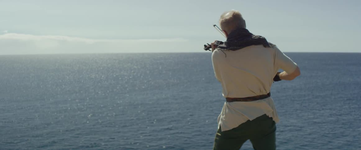 A man is playing a violin on the edge of a cliff