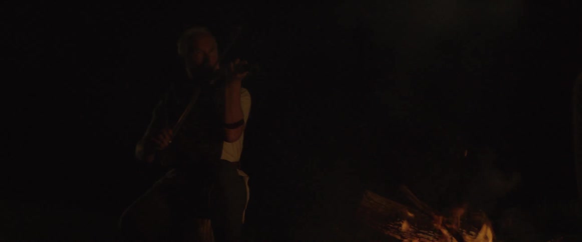 A man is playing the violin in the dark near a fire
