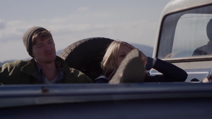 A man and woman sit in the back of a truck and talk