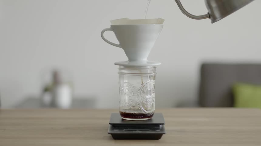 Hot water being poured from a tea kettle, through a funnel and into a mason jar