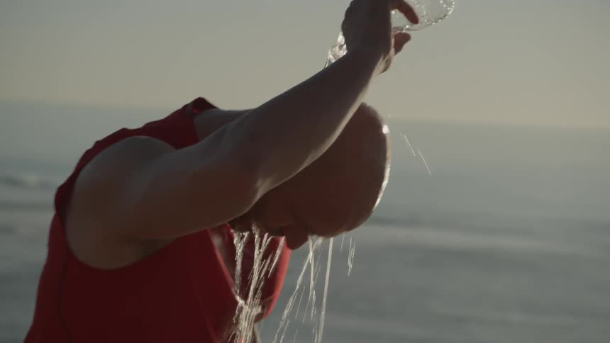 A man pours a water bottle over his head and looks down