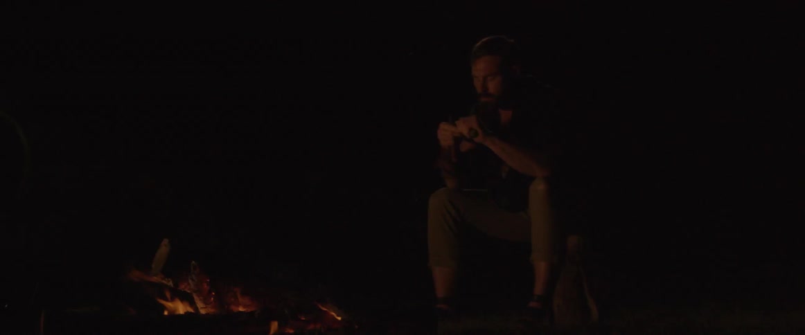 A man sits near the campfire at night