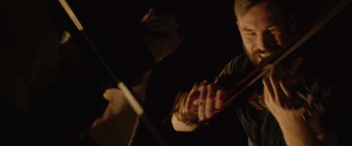 A man plays the violin in a very dark area
