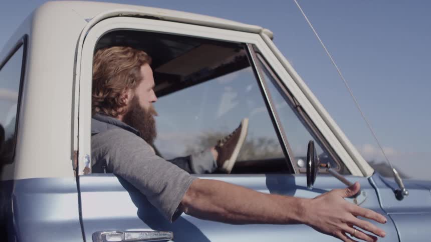 A man waves his hand out of the window of a moving blue truck