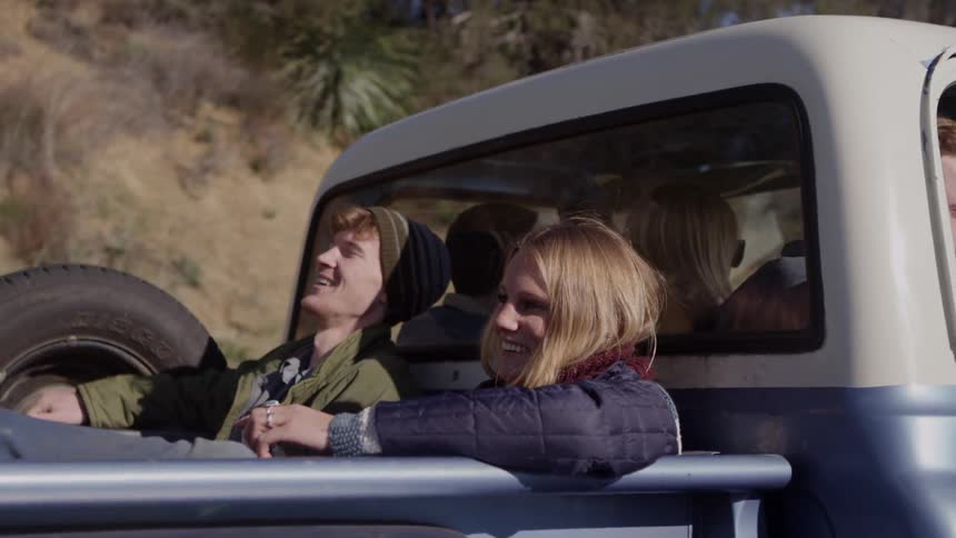 Three people are riding inside a pickup cab, while an additional man and a woman ride in the pickup bed