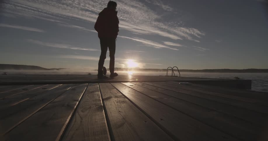 A man is walking on the lake harbor at dawn