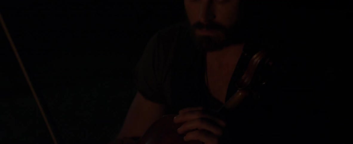 A man sits outside holding a violin at night