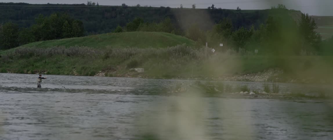 Birds fly over a river near a grassy hill