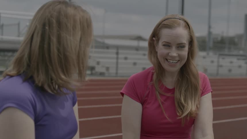 Two women laugh and talk at a track and field stadium