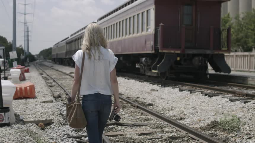 A woman holding a camera walks on old train tracks